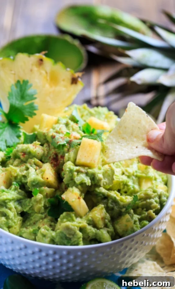Overhead shot of a full bowl of Spicy Pineapple Guacamole with a generously sized bowl of crispy tortilla chips, perfect for a party spread