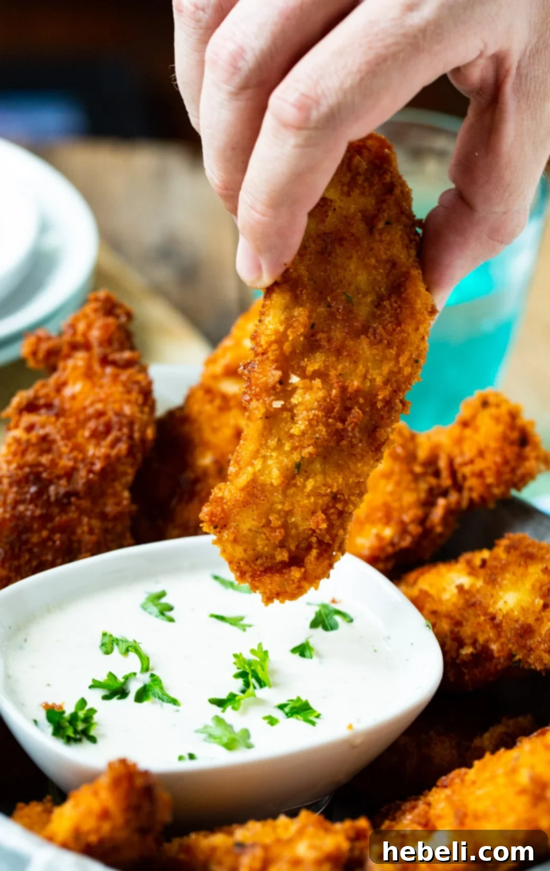 A crispy Ranch chicken finger being dipped into a bowl of creamy ranch dressing.