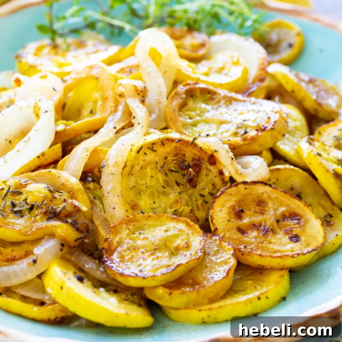 Close-up of golden brown pan-fried summer squash and onions on a serving platter, garnished with fresh herbs.