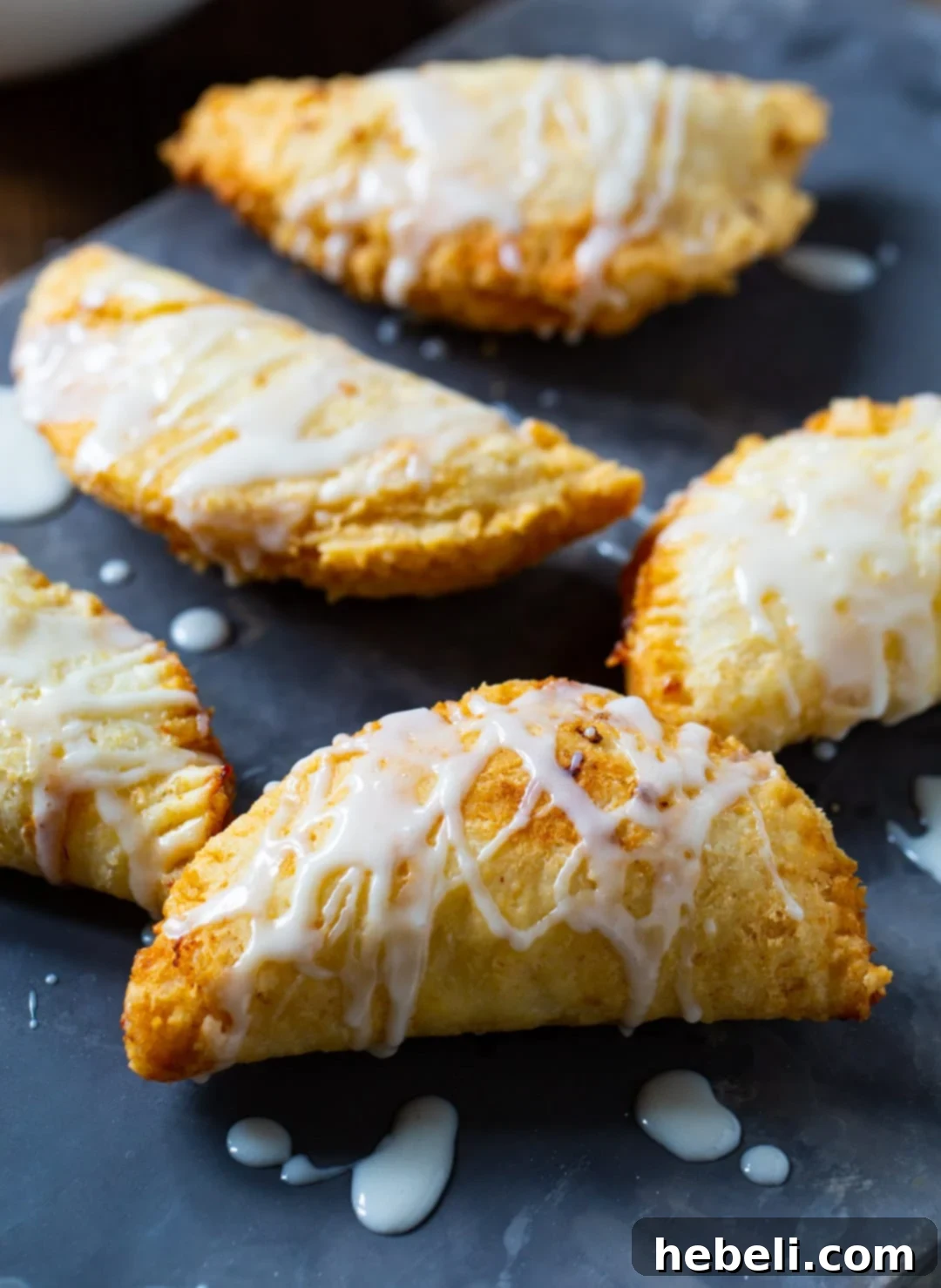 Golden Crispy Peach Turnovers 4 An overhead shot of several unbaked peach pies arranged on a baking sheet, showcasing their half-moon shape and crimped edges, ready for frying.