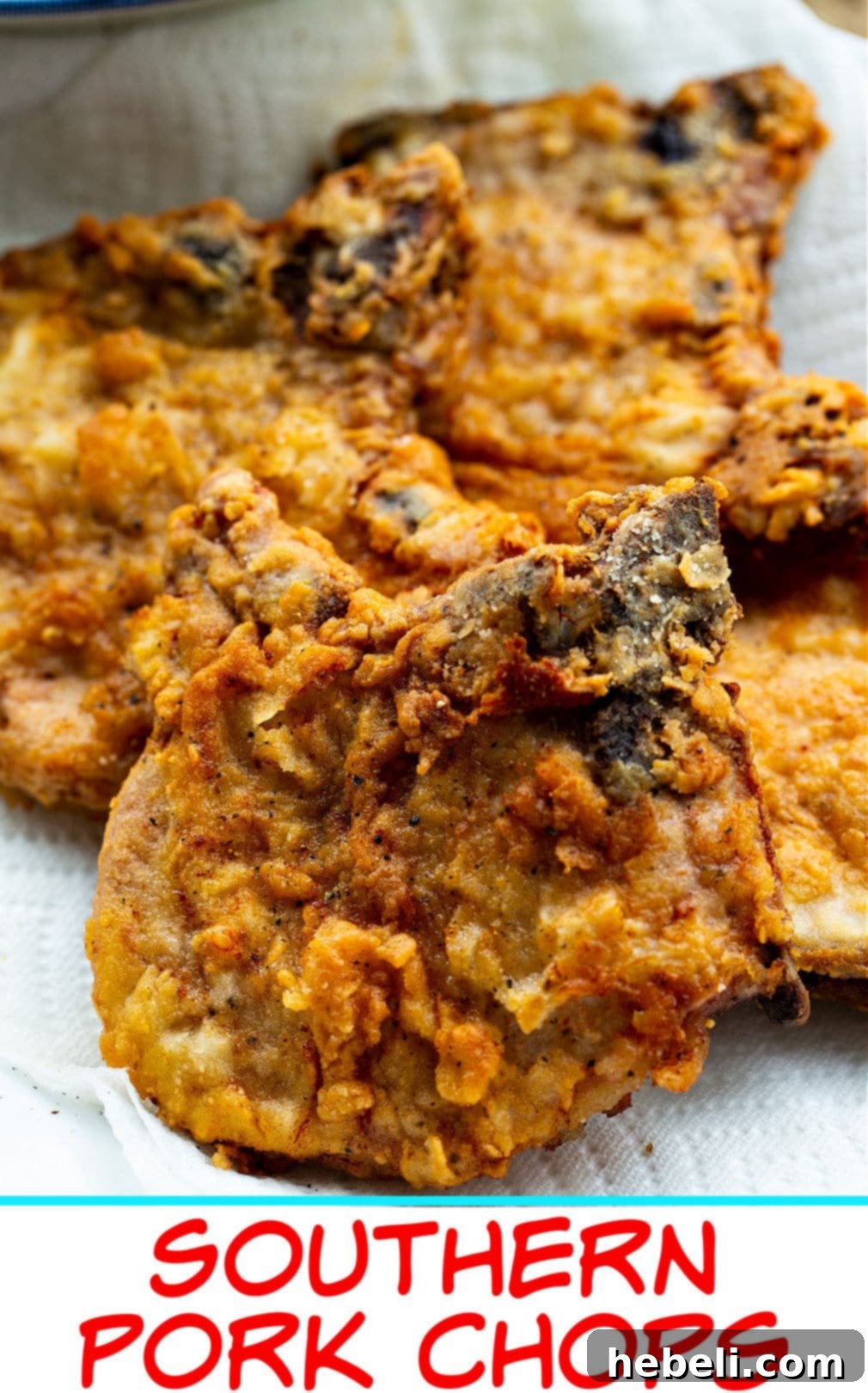 A stack of golden-brown Southern Fried Pork Chops resting on a paper towel-lined plate, absorbing excess oil after frying.