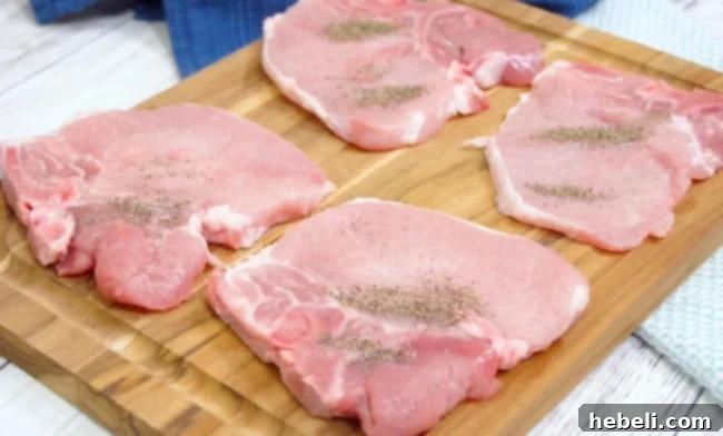 Seasoning raw pork chops with salt and pepper on a cutting board, preparing them for frying.