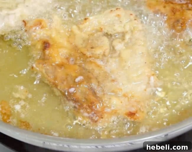 Two Southern Fried Pork Chops sizzling in hot oil in a cast-iron skillet, achieving a beautiful golden-brown color.