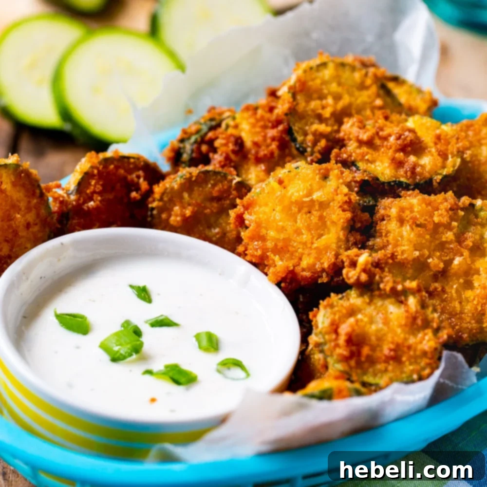 Golden Zucchini Crisps 2 Crispy Fried Zucchini Chips served in a blue basket with a bowl of ranch dressing.