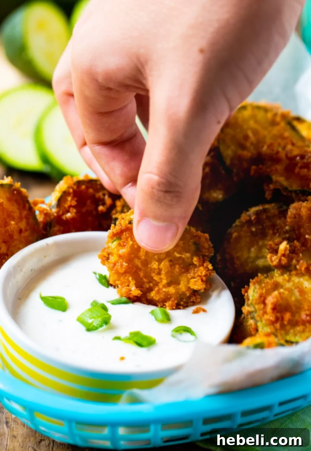 Golden Zucchini Crisps 7 A hand dipping a crispy fried zucchini chip into a bowl of creamy dip.