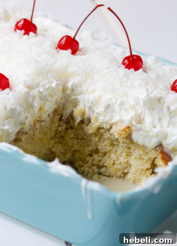 A beautifully decorated Pina Colada Poke Cake with whipped topping, shredded coconut, and maraschino cherries, presented on a vibrant blue plate.