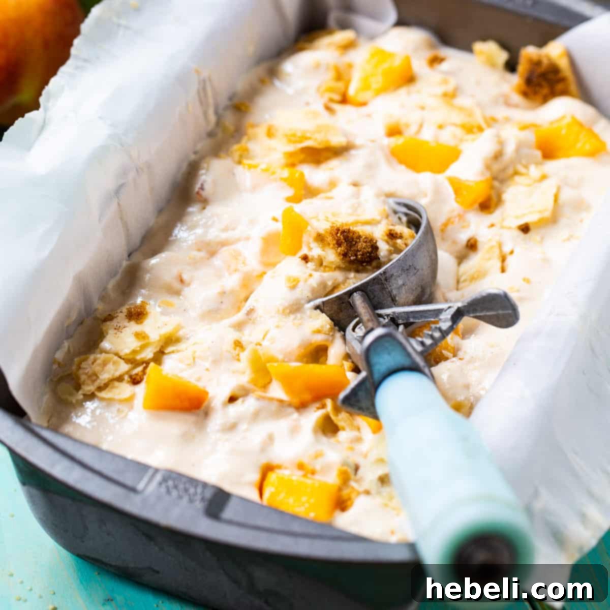 Creamy homemade Peach Cobbler Ice Cream in a 9x5-inch dish with an ice cream scoop, ready to be served.