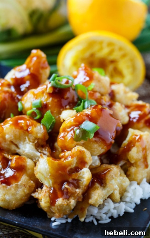 Golden-brown, crispy Orange Cauliflower florets glistening with the sweet and savory sauce, piled high on a plate.