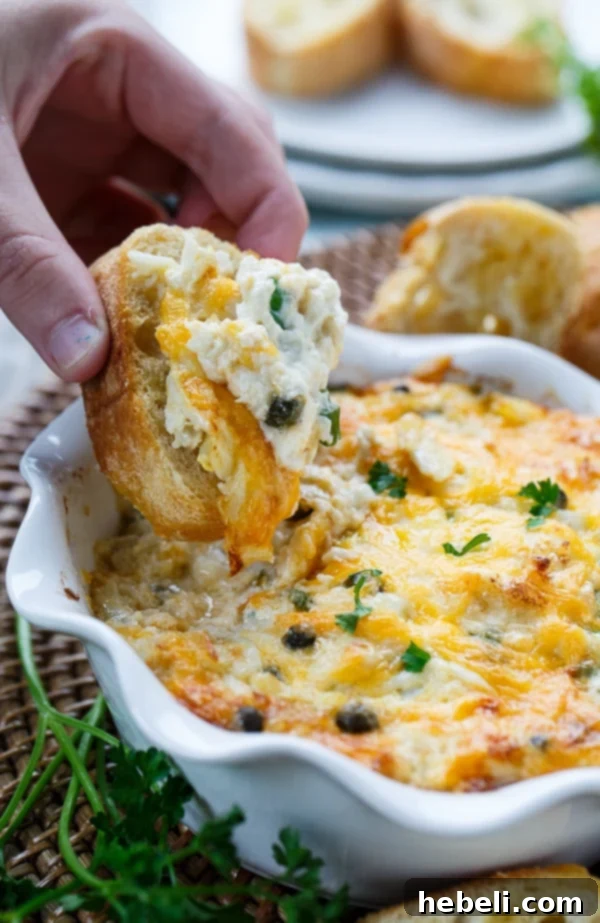 Incredible Hot Crab Dip made with crab meat, cream cheese, mayo, horseradish, capers, and cheddar cheese, served in a beautiful stoneware dish.