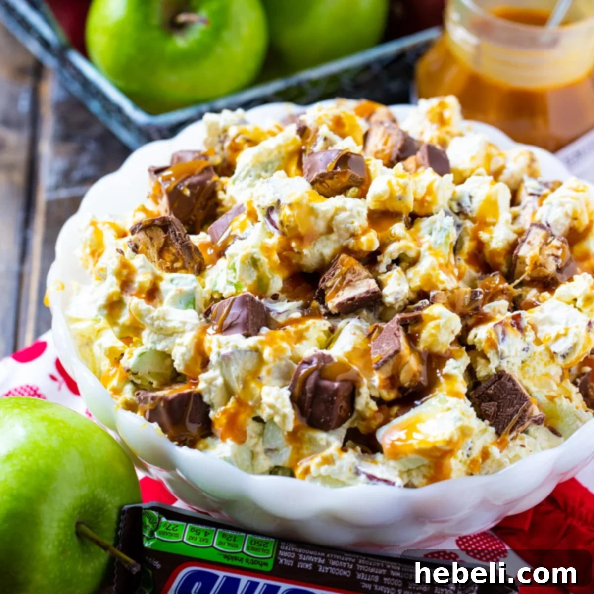 Creamy Snickers Caramel Apple Salad in a white serving bowl, garnished with caramel drizzle and chopped Snickers.