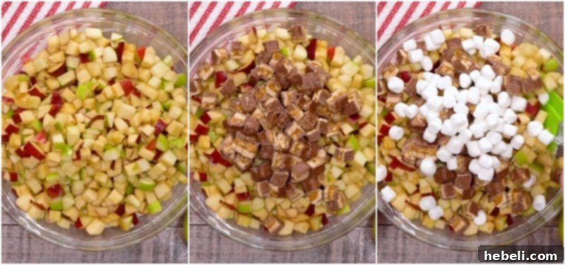Hands folding chopped apples, Snickers, and marshmallows into the creamy pudding mixture.