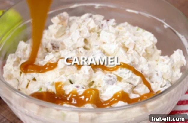 Caramel sauce being drizzled over the finished Snickers Caramel Apple Salad in a serving bowl.