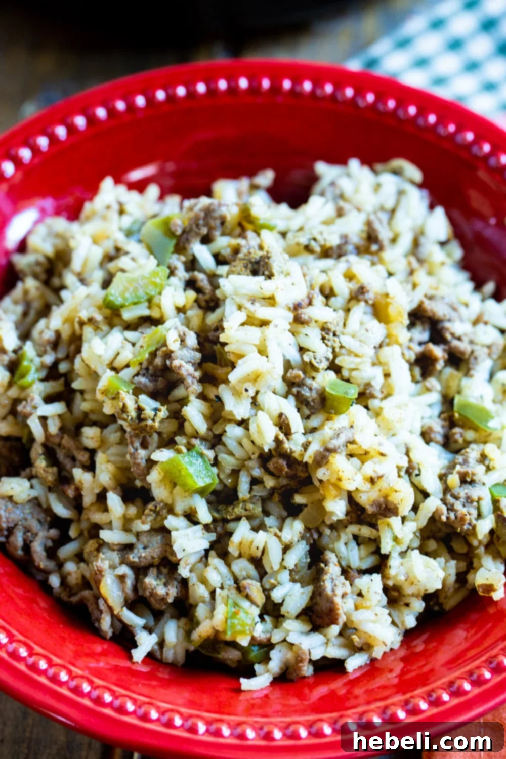 A vibrant close-up of a serving of Dirty Rice in a rustic red bowl, with a fork ready to dig in, showcasing its rich texture and color.