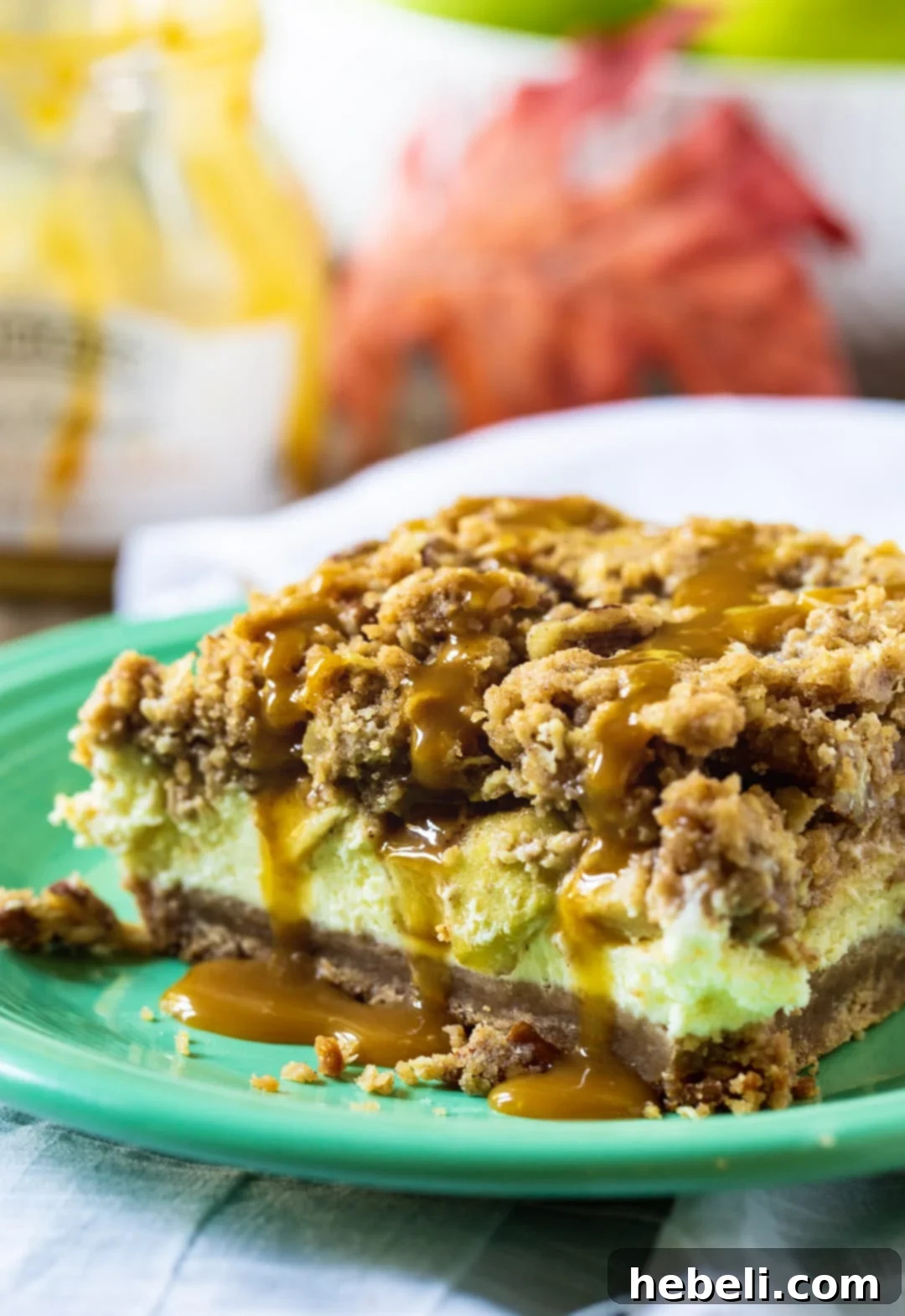 Close-up shot of a single Caramel Apple Cheesecake Bar, highlighting the crumbly streusel topping and the glistening caramel sauce drizzle cascading over it.