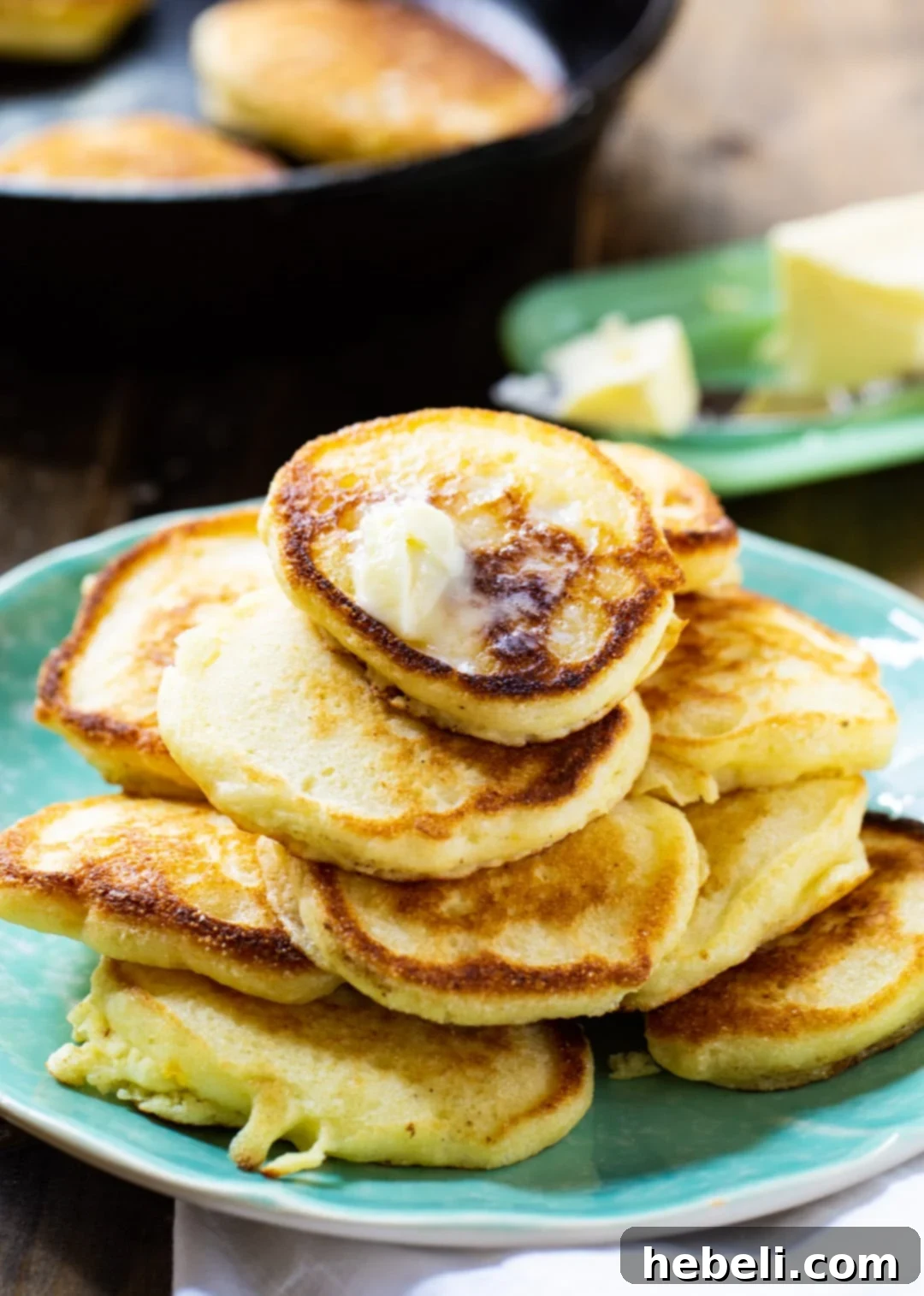 Hoe Cakes on a plate with cast iron pan in background.