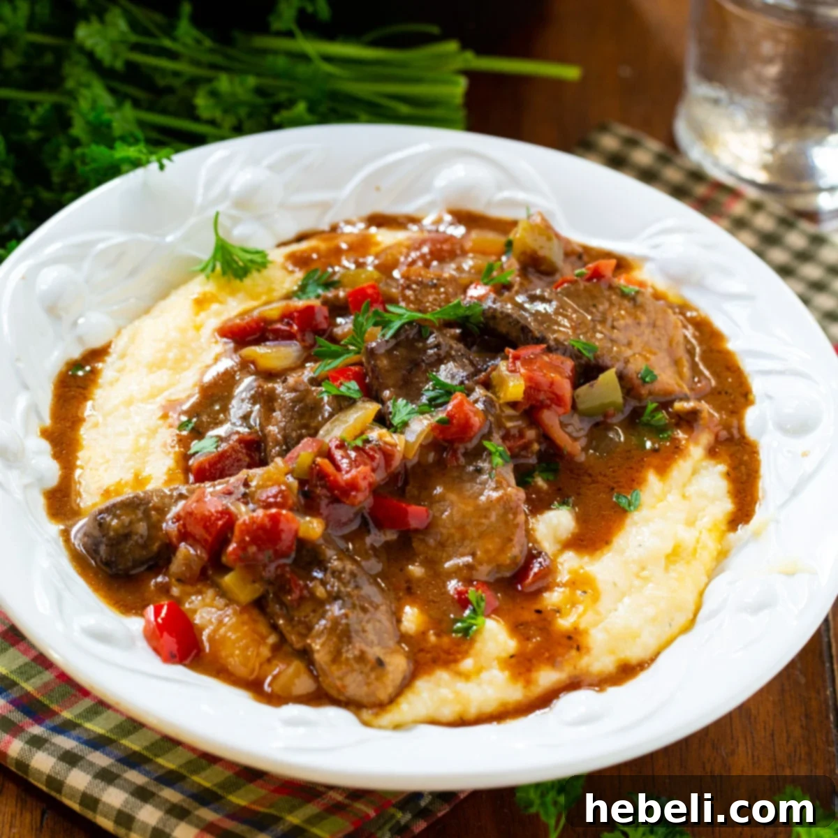 A serving of Grillades and Grits, featuring tender beef in a rich red gravy, artfully arranged over creamy grits in a pasta bowl.