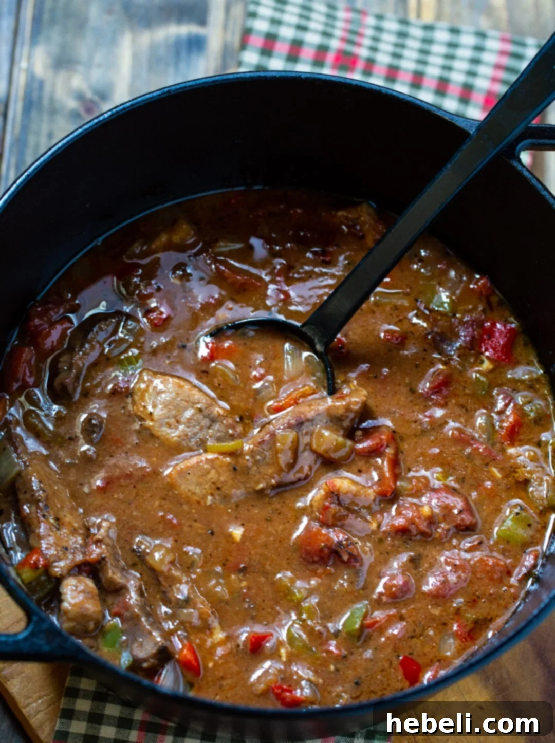 Slices of tender Grillades simmering in a rich, red gravy within a cast iron pot, showcasing the slow-cooked goodness.