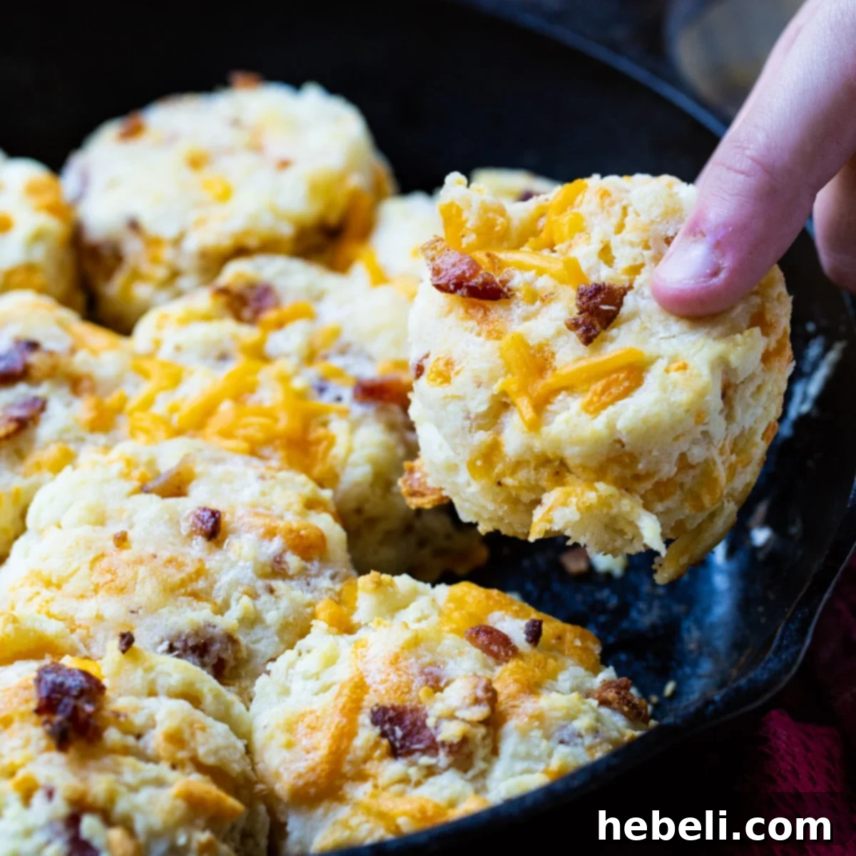 Cheddar Bacon Delights 2 Hand picking up a golden-brown Bacon Cheddar Biscuit, highlighting its fluffy texture and savory additions.