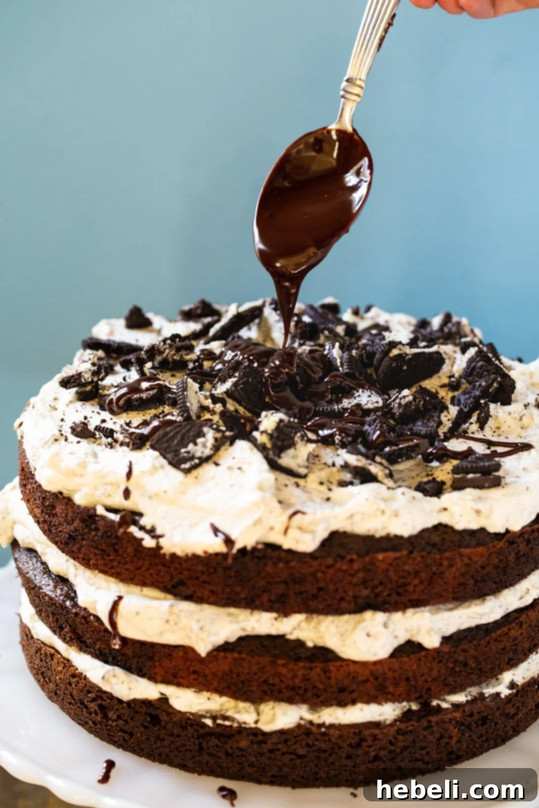 A spoon expertly drizzling melted chocolate ganache over a slice of Mississippi Mudslide Cake, highlighting its rich layers and creamy filling.