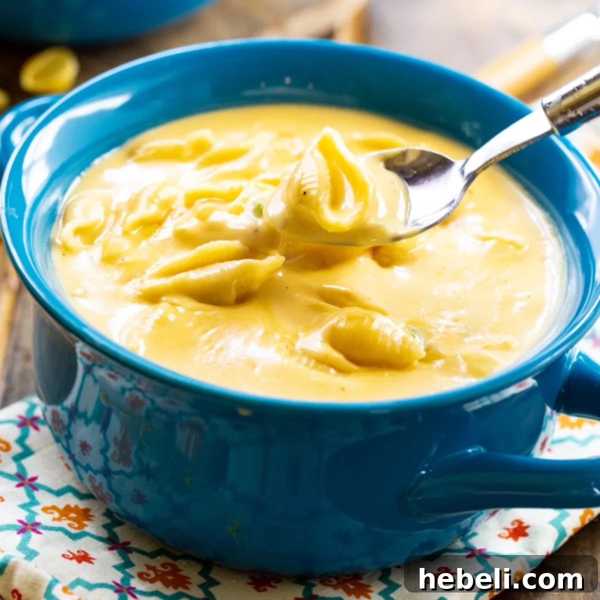 A vibrant blue bowl filled to the brim with creamy Mac and Cheese Soup, showcasing tender pasta shells in a rich, golden broth.