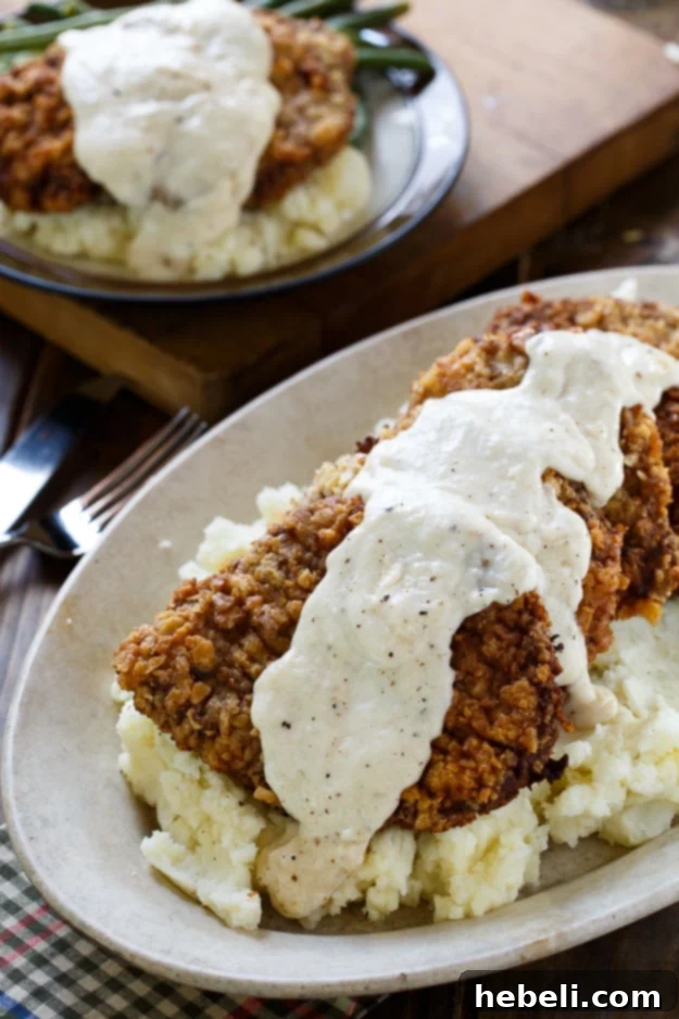 Several pieces of Chicken Fried Steak piled high, generously topped with white gravy