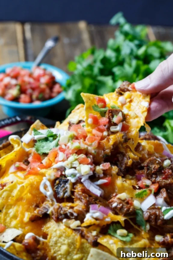Ultimate Brisket BBQ Nachos 6 Overhead shot of BBQ Brisket Nachos in a cast iron skillet, with a scoop of sour cream and fresh toppings.
