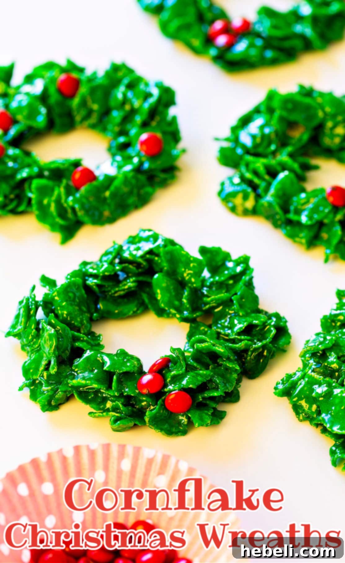 Wreath cookies on a white background, some with red M&Ms, others with red hot candies, showcasing their vibrant holiday appeal.