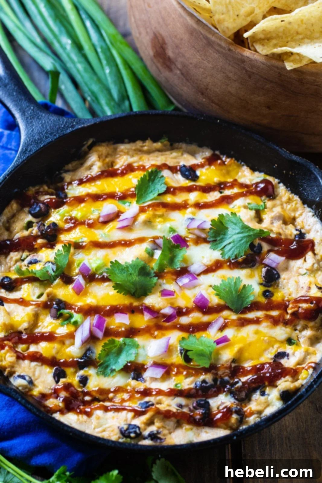 Ultimate BBQ Chicken Dip 3 Close-up of baked BBQ Chicken Dip in a skillet, garnished with fresh green onions and served with an abundance of tortilla chips.