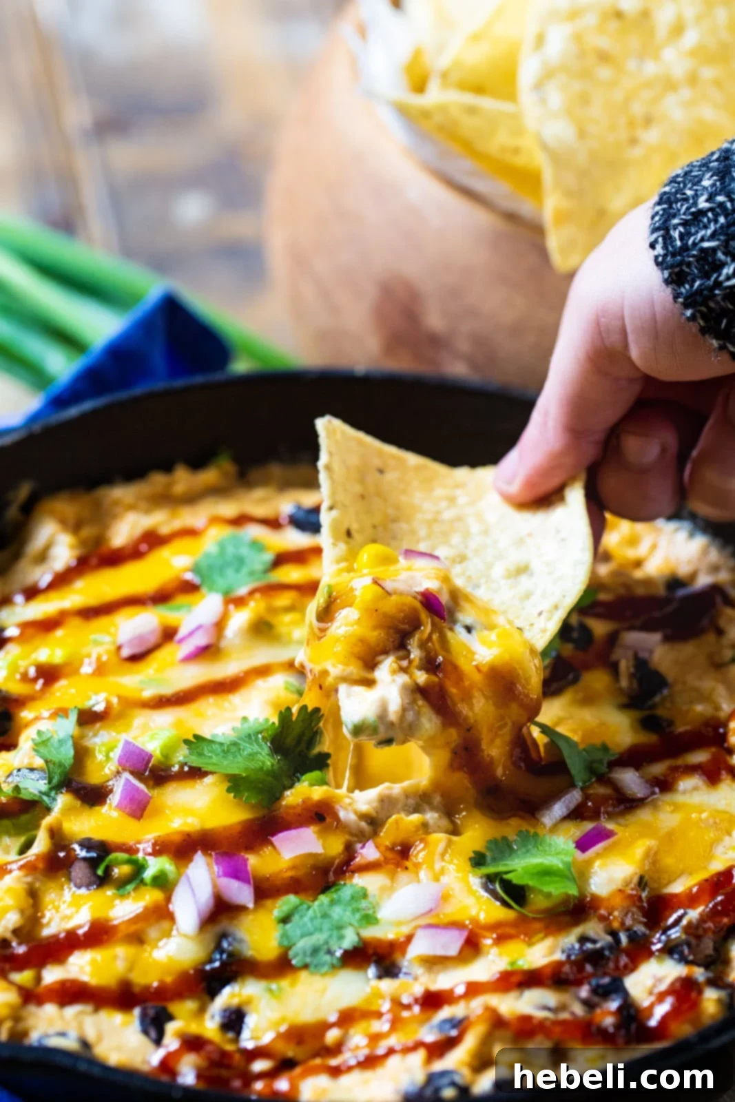 Ultimate BBQ Chicken Dip 4 A tortilla chip scooping up a generous portion of warm, cheesy BBQ Chicken Dip from a skillet, highlighting its delicious texture.