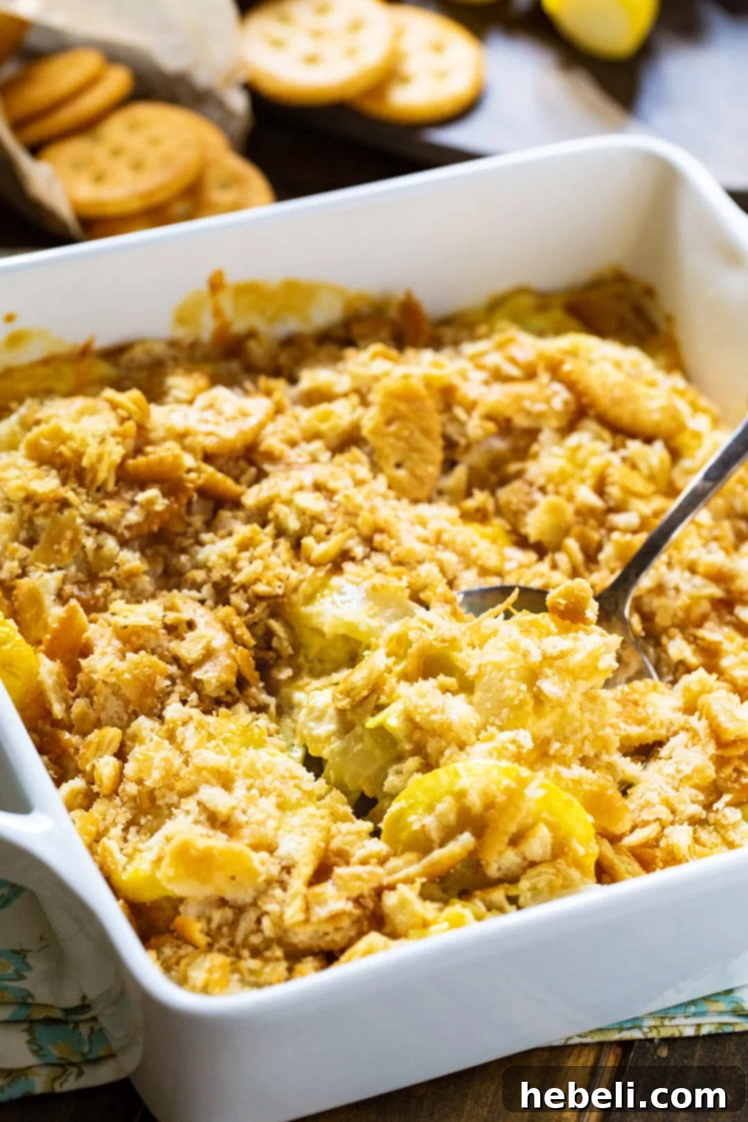 A serving spoon scooping a portion of Yellow Squash Casserole out of a baking dish, showing its creamy texture and cheesy interior.