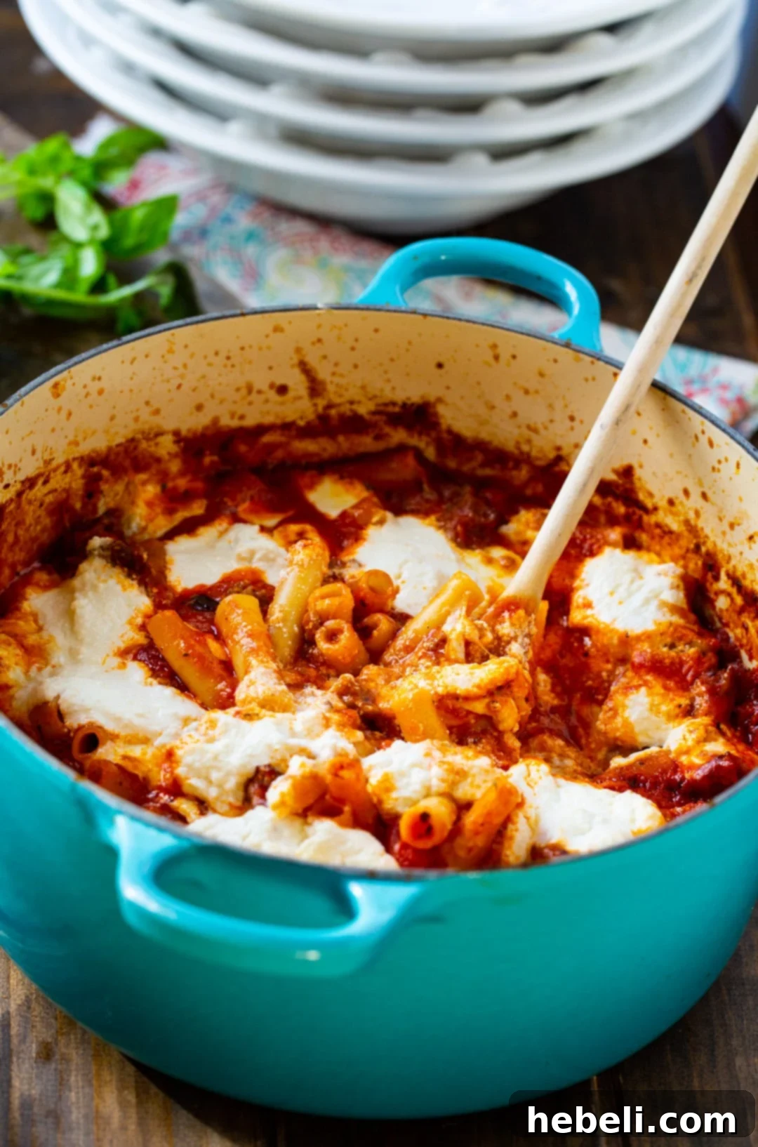 Wooden spoon scooping a generous serving of One-Pot Ziti from a Dutch oven.
