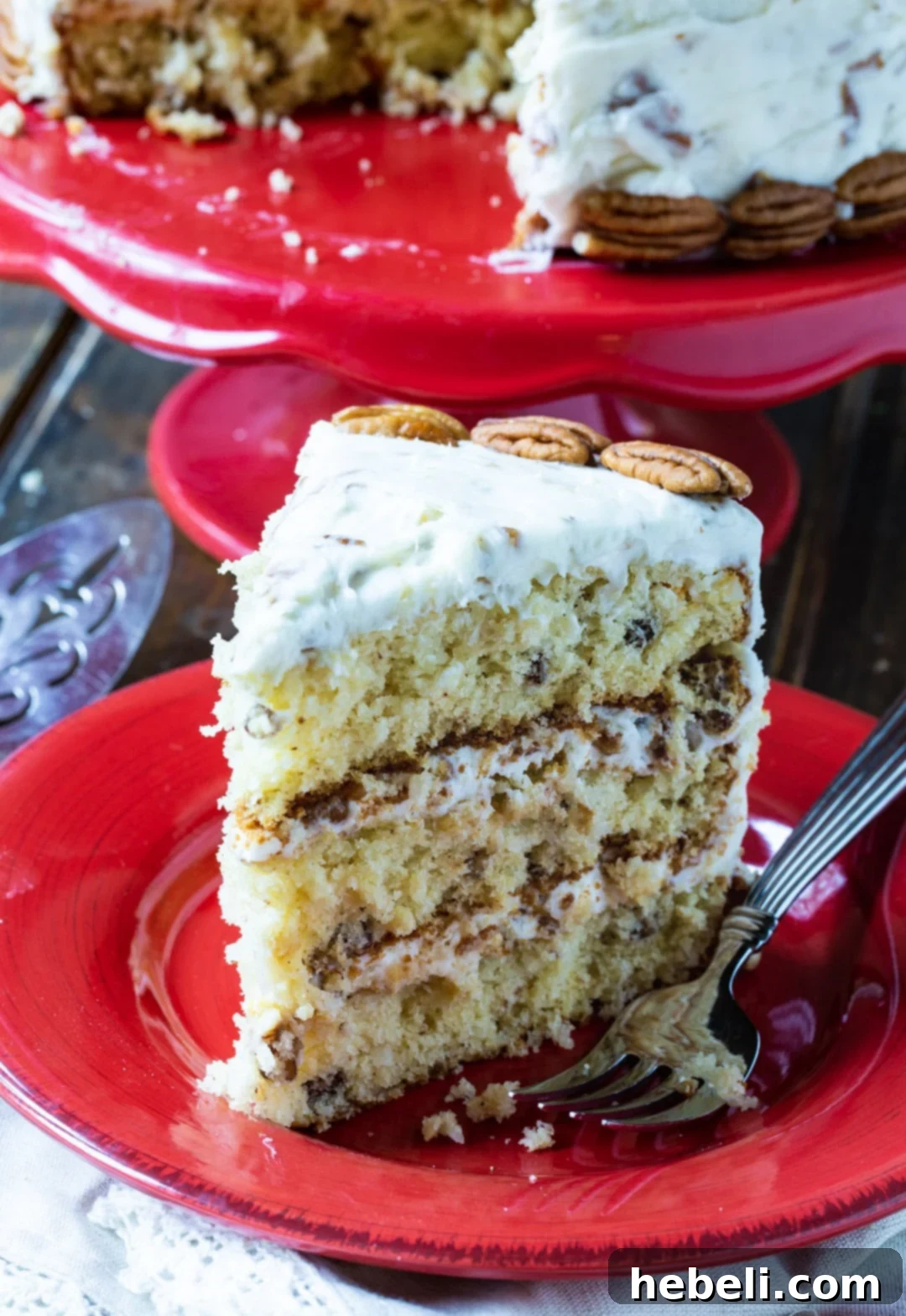 A perfect slice of Italian Cream Cake, revealing its moist layers, coconut, pecans, and creamy frosting, served on a red plate.