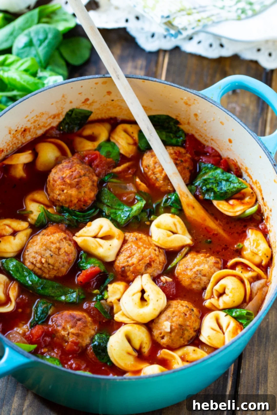 A ladle serving Meatball and Tortellini Soup from a Dutch oven.