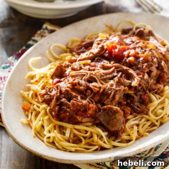Tender Slow Cooker Short Rib Sauce served over pasta, garnished with fresh herbs