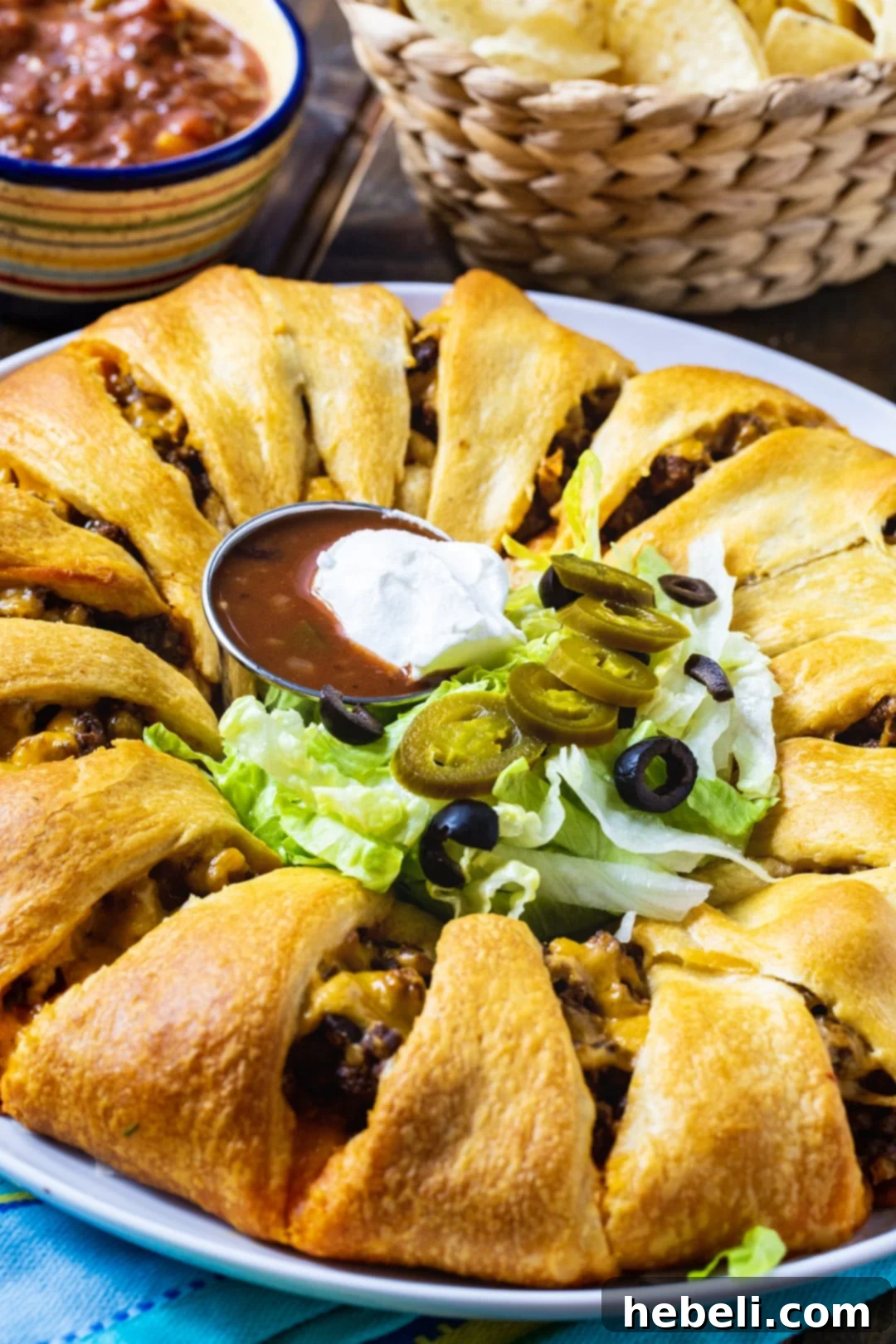 Fiesta Taco Wreath 6 A fully baked Taco Ring on a plate, beautifully garnished with fresh lettuce, black olives, and a dollop of vibrant salsa in the center, ready to be served as an appetizer.