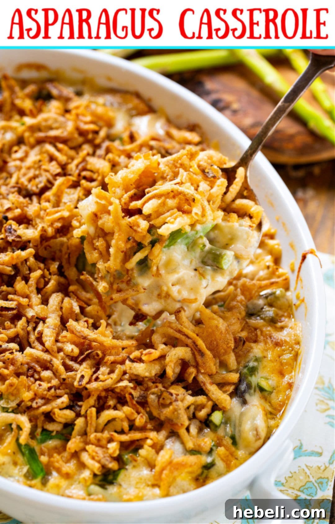 A large serving spoon scooping out a portion of warm Asparagus Casserole from a baking dish.