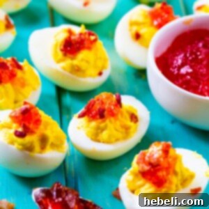 Red Pepper Jelly Deviled Eggs with Bacon on a light blue background.