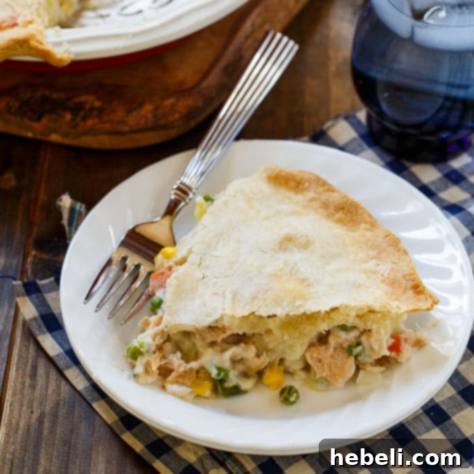 A delicious Salmon Pot Pie with a golden, flaky crust, served on a rustic wooden board. The filling is thick and creamy, showcasing salmon and various vegetables.