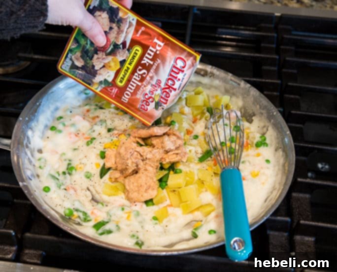 A side shot of a slice of Salmon Pot Pie, revealing the rich, creamy filling packed with salmon chunks, carrots, and peas. The crust is golden and flaky.