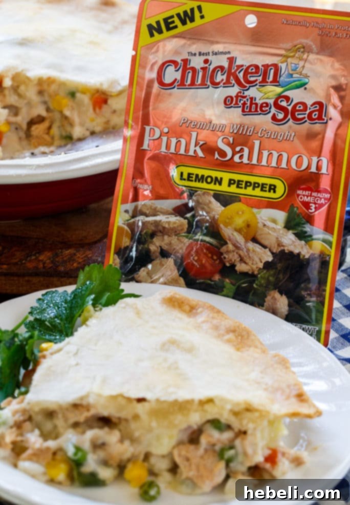 An overhead shot of the Salmon Pot Pie, showcasing the intricate crimped edges of the golden crust. A single slice has been removed, revealing the steaming, chunky filling.