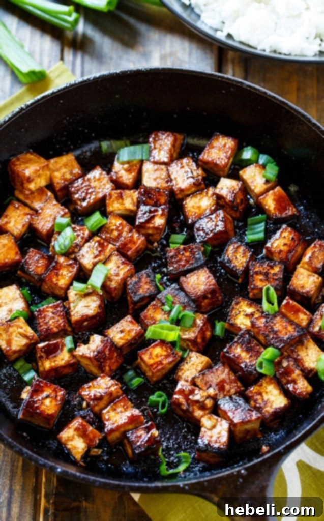 Close-up of perfectly seared Asian Garlic Tofu pieces in a skillet, showcasing their golden-brown crisp exterior.