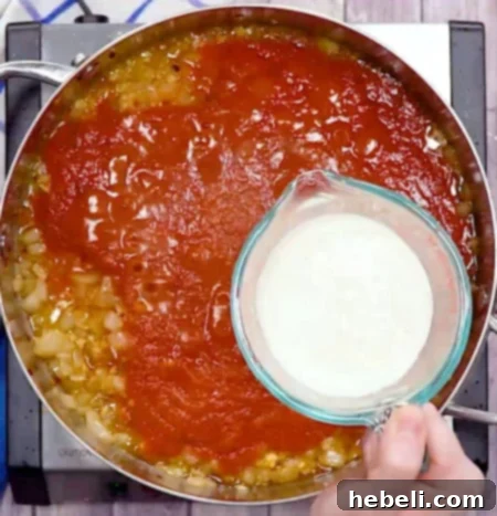 Spicy Shrimp Rose Pasta 7 Pouring rich heavy cream into the simmering tomato sauce, enhancing its richness.