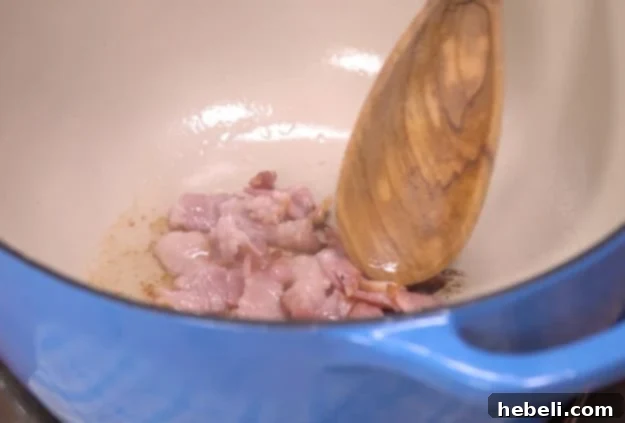 Cooking crispy bacon pieces in a Dutch oven until golden brown.