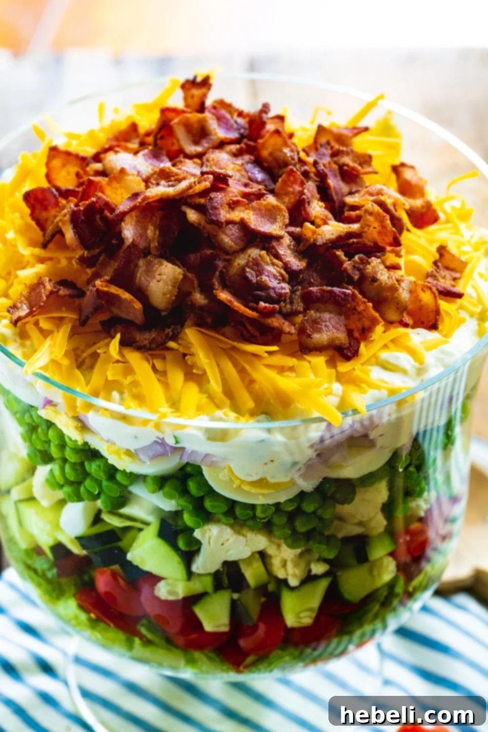 Layered Salad with cheddar cheese and crispy bacon topping in a clear trifle dish.