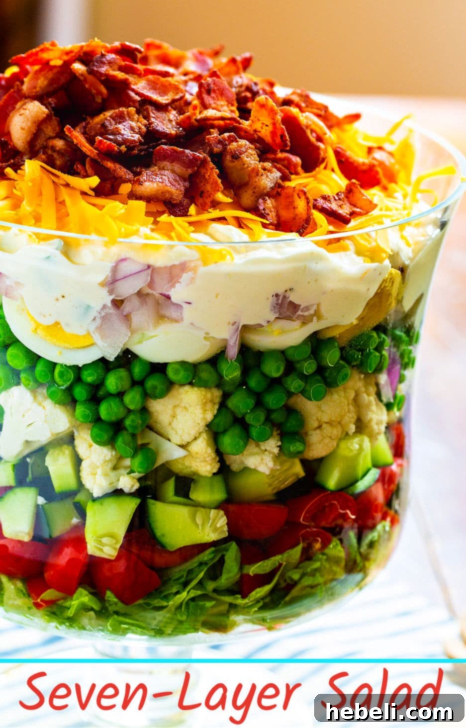 Classic Seven-Layer Salad topped with a creamy dressing, bacon, and shredded cheddar cheese, ready to serve.