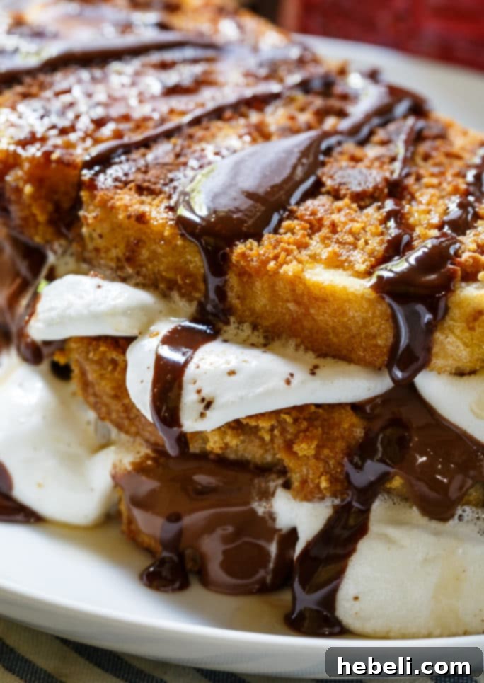 Two generous servings of S'mores French Toast on white plates, topped with maple syrup and extra marshmallows for garnish