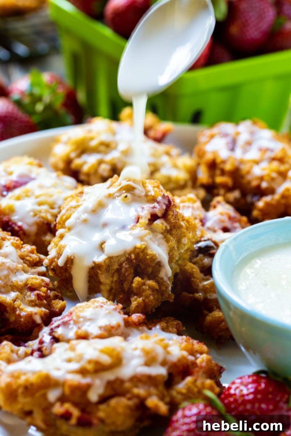 Sweet Strawberry Fritter Delights 4 A spoon delicately drizzling a thick, white glaze over warm Glazed Strawberry Fritters, highlighting their crisp exterior.