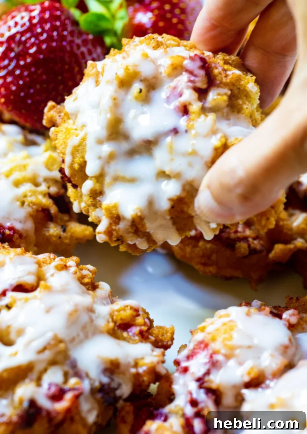 Sweet Strawberry Fritter Delights 5 A hand reaching for a Glazed Strawberry Fritter from a plate, illustrating its irresistible appeal.