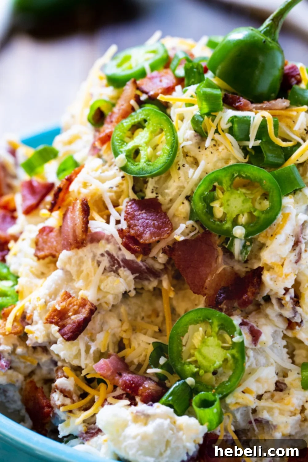 Close-up view of creamy Jalapeno Popper Potato Salad, generously covered with vibrant green fresh jalapeno slices and crispy crumbled bacon bits.