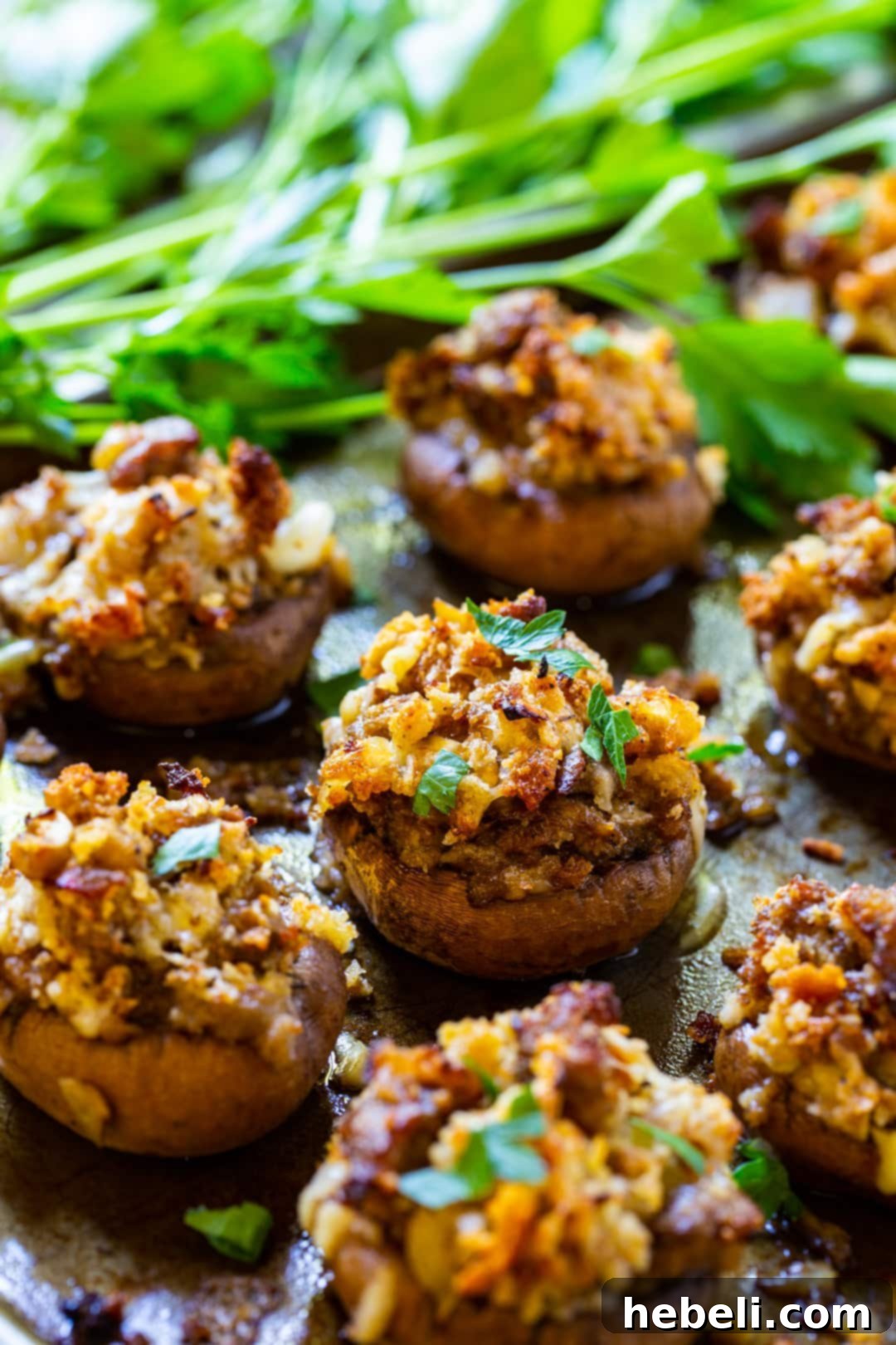 Mushrooms stuffed with a savory sausage filling, garnished with fresh parsley on a baking sheet.